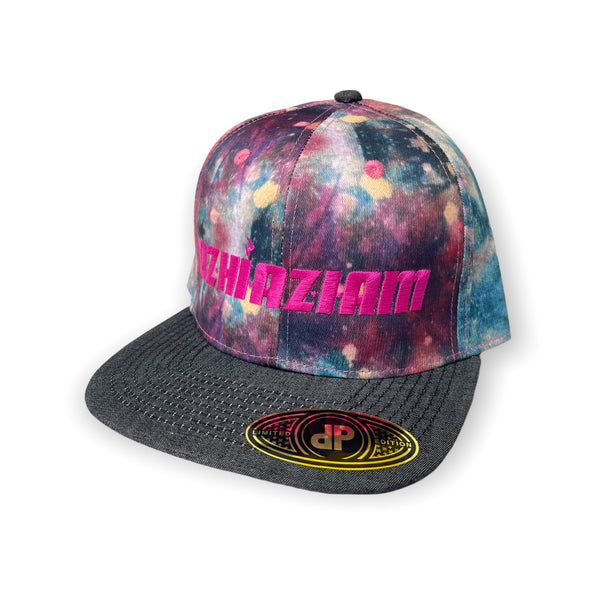 A photo of Azhiaziam's Denim Tye Dye Hat featuring a tie-dye pattern on a denim fabric. The hat has a flat bill and an adjustable snap back closure. Hot pink embroidered "Azhiaziam" on front panel.